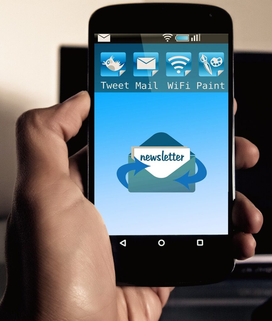 A hand holding a smartphone with a large "newsletter" envelope icon on the screen below smaller icons.