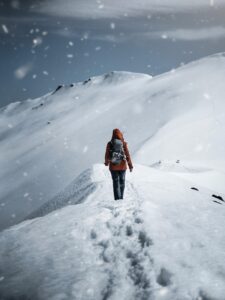 A woman walking on a snowy mountain top; from a distance, her feet have left deep imprints in the snow.